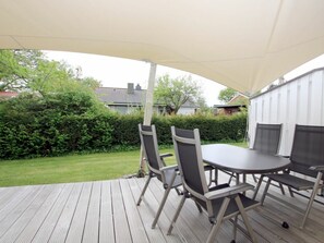 An outdoor patio with a table and chairs, a canopy overhead, and a view of a garden and buildings in the background. - Cockle at Susanne-fischer-weg 53 (Wyk auf Foehr)