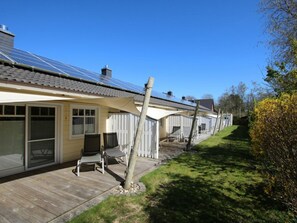 Una hilera de casas con paneles solares, una terraza de madera y una zona con césped.