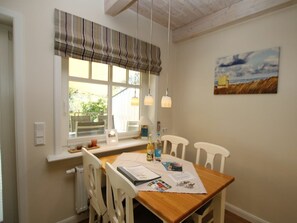 A dining area with a wooden table, white chairs, a window with a striped valance, and a painting on the wall. - Cockle at Susanne-fischer-weg 53 (Wyk auf Foehr)