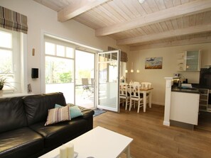A modern living room with a black leather sofa, a white coffee table, and a dining area with white chairs and a table. - Cockle at Susanne-fischer-weg 53 (Wyk auf Foehr)