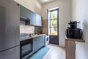 A compact kitchen with a washing machine, a coffee machine, and a large window. - ZAGARA DI MARE (Palermo)