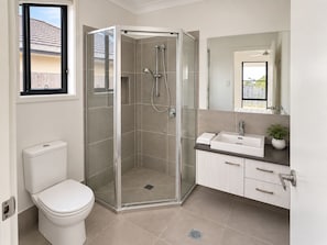 A modern bathroom with a glass-enclosed shower, a toilet, a sink, and a mirror. - The Amber House | Modern Family Retreat (Ormeau)