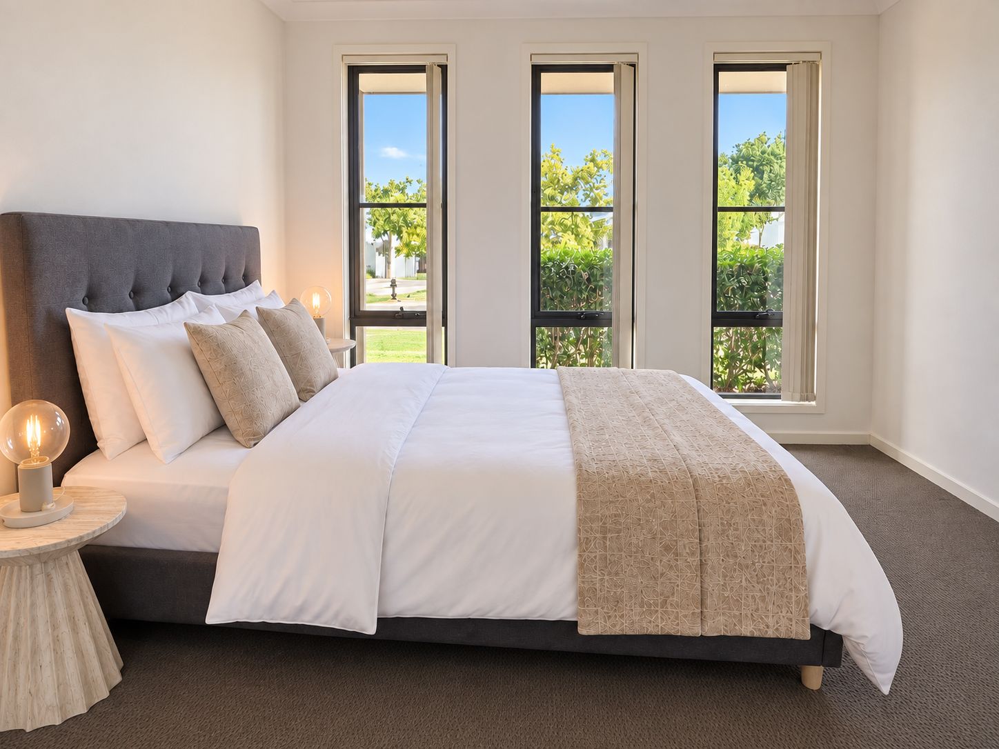 Une chambre à coucher avec un grand lit, une table de chevet avec une lampe et trois fenêtres donnant sur un paysage verdoyant.