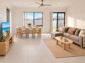 A modern living room with a dining area, a sofa, a coffee table, and a TV on a wooden stand. - The Amber House | Modern Family Retreat (Ormeau)