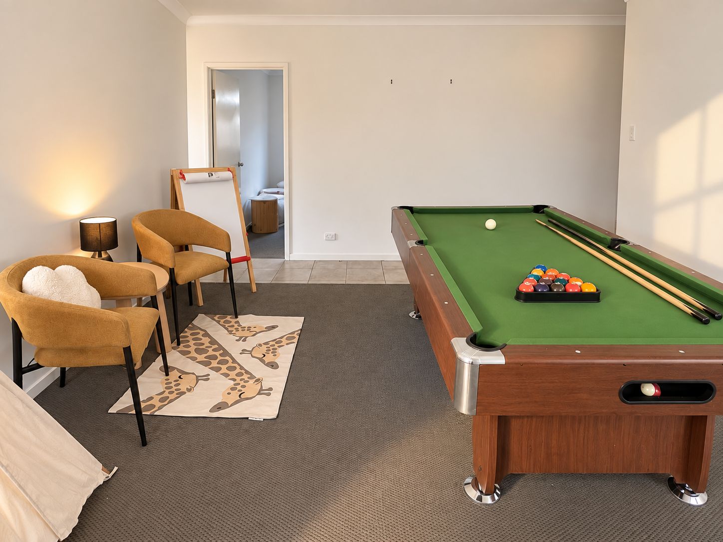 A pool table with balls and cues, two chairs, a lamp, and a giraffe-patterned rug.