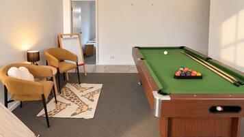 A pool table with balls and cues, two chairs, a lamp, and a giraffe-patterned rug.