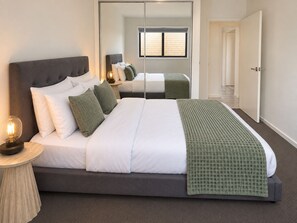 A modern bedroom with a large bed, a bedside lamp, and a mirror. - The Amber House | Modern Family Retreat (Ormeau)