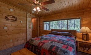 Ein Schlafzimmer einer Holzhütte mit Bett, Deckenventilator, Fenster und Nachttisch.