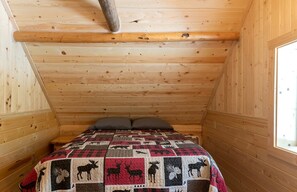 Une chambre dans une cabane en bois, avec un lit, des oreillers et une courtepointe ornée de motifs représentant des animaux.