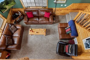 A cozy cabin interior with a brown leather sofa, a wooden coffee table, and a rustic wooden chair. - Scenic Island Park Cabin with Private Hot Tub & ATV Access Near Yellowstone, Idaho (Island Park)