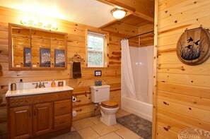 A wooden cabin bathroom with a wooden vanity, a toilet, a bathtub, and a shower curtain. - Scenic Island Park Cabin with Private Hot Tub & ATV Access Near Yellowstone, Idaho (Island Park)