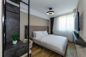 A modern hotel room with a large bed, a bedside table, a potted plant, a wall-mounted TV, and a ceiling light fixture. - Khotel Temel Chorlu (Çorlu)