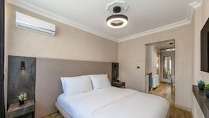 Una habitación de hotel moderna con una cama grande, una mesita de noche con lámpara, un equipo de aire acondicionado y un aplique de techo.
