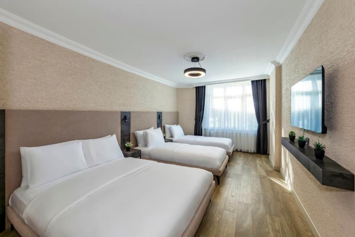 A hotel room with two beds, a flat-screen TV mounted on the wall, and a window with curtains.