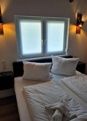 A hotel room with a large bed, two bedside tables, a window with blinds, and wall-mounted lights. - Holiday Home in Walkenried With Barbecue (Walkenried)