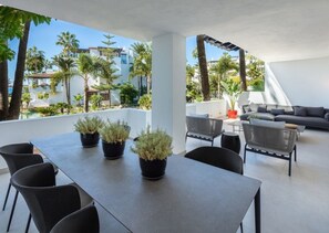Zona d'estar exterior moderna amb taula i cadires, envoltada de plantes en testos i vista a una zona residencial.