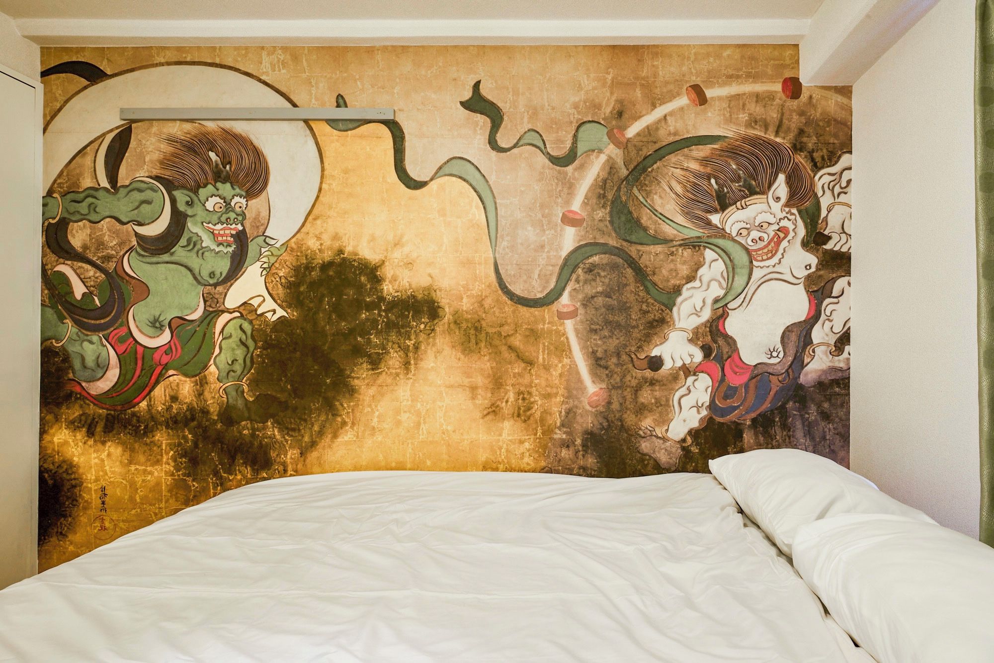 A bed with a plain white mattress and pillows, and a wall with a mural of two mythical creatures.