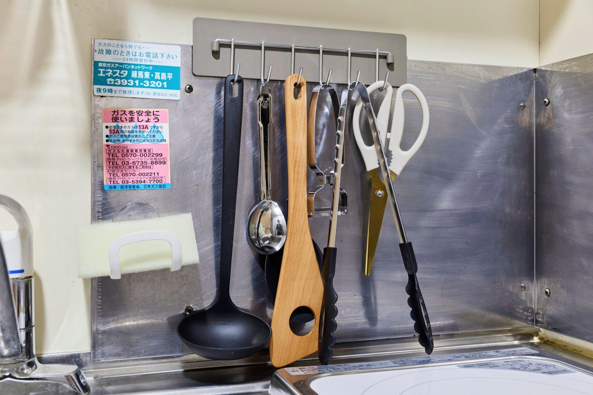A kitchen area with various utensils hanging on a rack, including a ladle, a wooden spoon, and a pair of scissors.