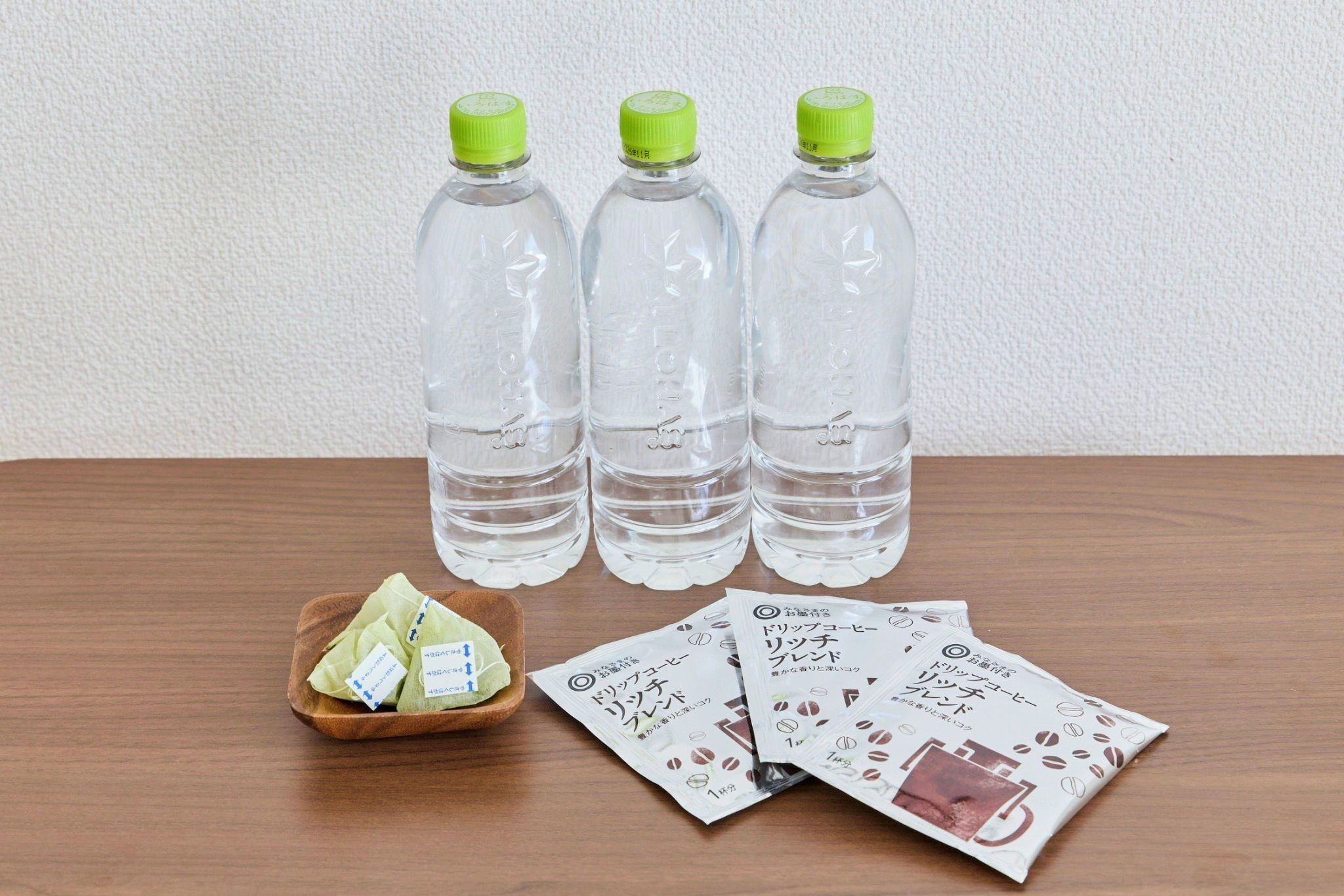 Three clear plastic bottles with green caps, a wooden tray with green tea bags, and a white wall in the background.