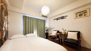 A hotel room with a large bed, a desk with a chair, a small table with a plant, and a window with curtains. - Vrbo Property (板橋区)