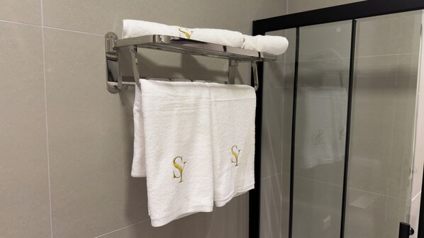 Un baño con un toallero que sostiene dos toallas blancas con letras doradas.