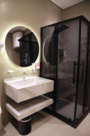 Un baño moderno con lavamanos de mármol blanco, un espejo redondo y ducha con cerramiento de vidrio.