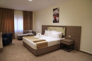 Una habitación de hotel con una cama grande, una mesita de noche, una silla, un sofá y un cuadro en la pared.