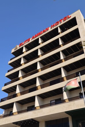 Un edificio de hotel con un letrero que dice 'ELITE AMMAN HOTEL' y un asta con una bandera.