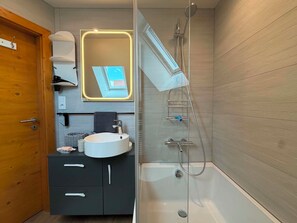 A modern bathroom with a glass-enclosed shower, a white sink, and a mirror with a lighted frame. - Vrbo Property (Gertwiller)