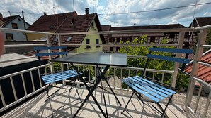 En udendørs terrasse med et bord og bænke, omkranset af gelænder, med huse i baggrunden.