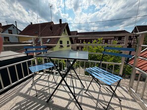 An outdoor patio with a table and benches, surrounded by a metal railing, with houses in the background. - Vrbo Property (Gertwiller)