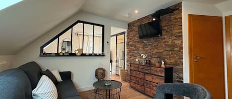 A modern living room with a sloped ceiling, a stone fireplace, a flat-screen TV, and a large mirror.
