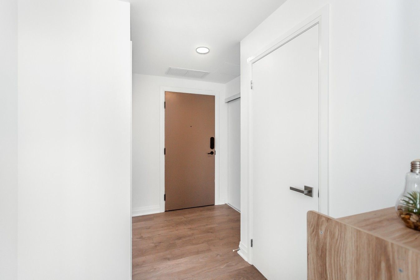 A hallway with a wooden floor, white walls, and a door at the end.
