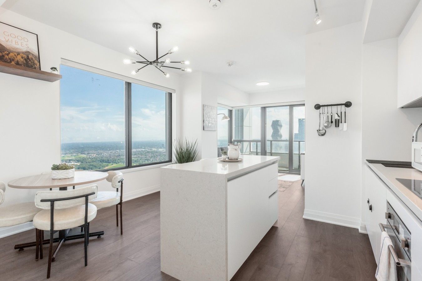A modern kitchen with a large island, a dining area with a view, and a kitchen with hanging utensils.