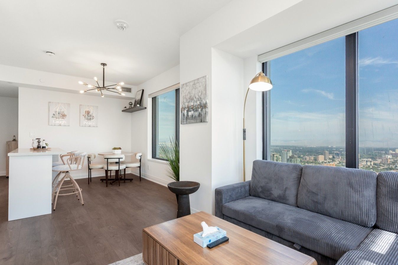 A modern living space with a dining area, a sofa, and a large window offering a city view.