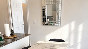 A dining area with a marble table, four chairs, a mirror, and a kitchen visible through an open door. - High-Rise 3BR Oasis | Free Parking | City Views (Mississauga)