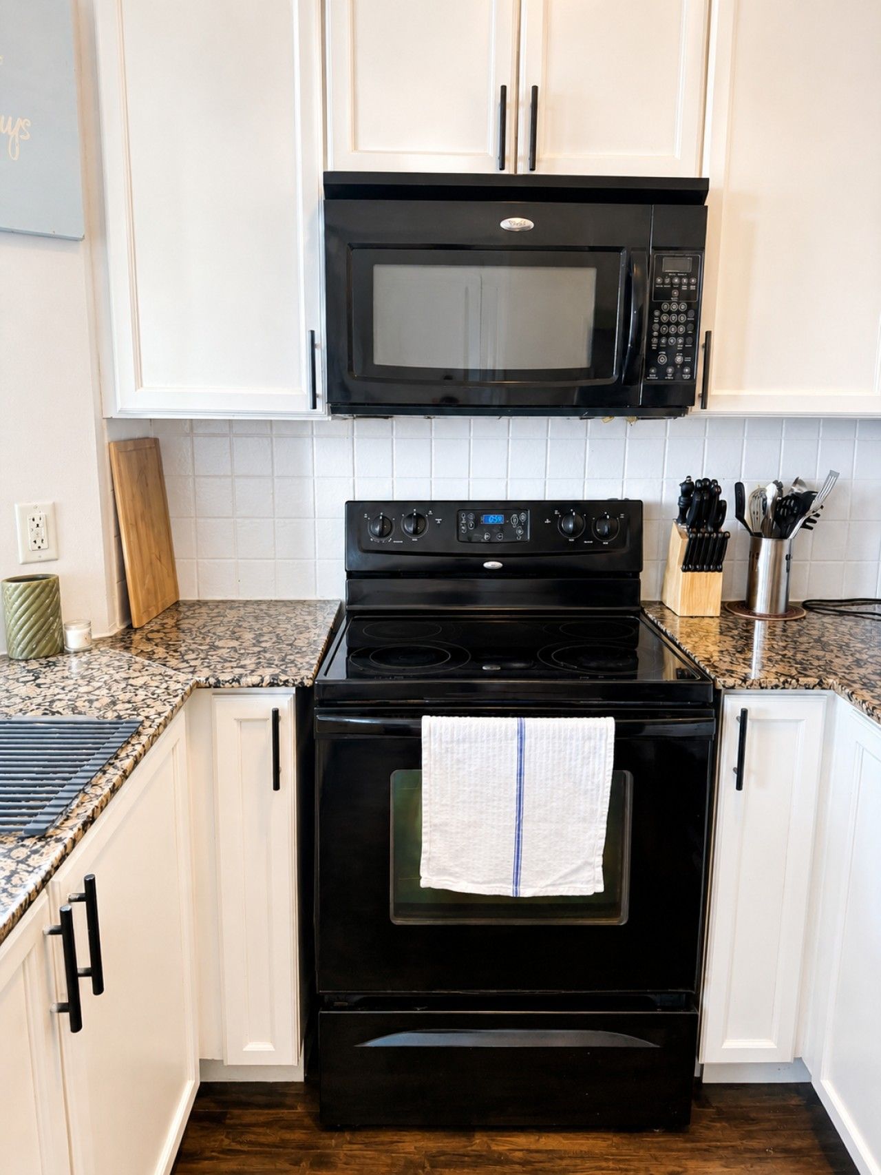 A kitchen with white cabinets, a black microwave, and a stove.