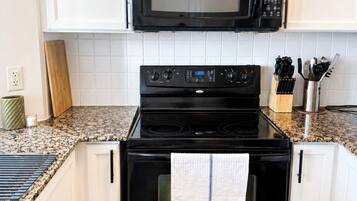 A kitchen with white cabinets, a black microwave, and a stove.