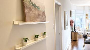 Un couloir aux murs blancs, doté d’un plancher en bois et orné d’un tableau au-dessus d’une étagère. Trois petites plantes en pot sont disposées sur l’étagère.
