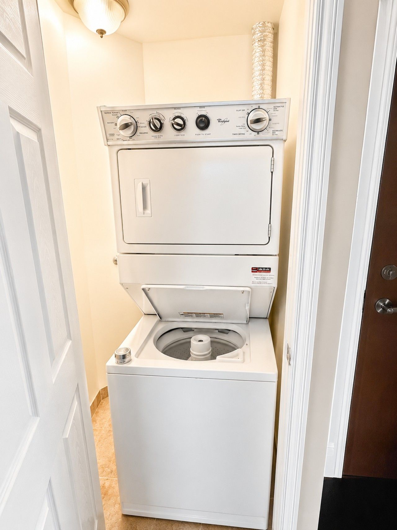 Un appareil compact combinant lave-linge et sèche-linge, à deux portes, installé dans une petite buanderie dont le sol est carrelé.