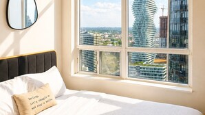 A hotel room with a large bed, a view of modern buildings, and a mirror on the wall. - High-Rise 3BR Oasis | Free Parking | City Views (Mississauga)