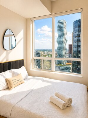A hotel room with a large bed, a view of modern buildings, and a mirror on the wall. - High-Rise 3BR Oasis | Free Parking | City Views (Mississauga)
