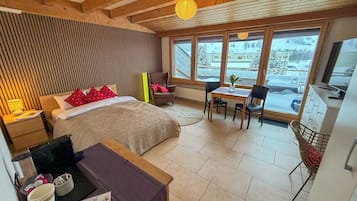 Una habitación de hotel con cama, escritorio y vista a un paisaje nevado a través de amplias ventanas.