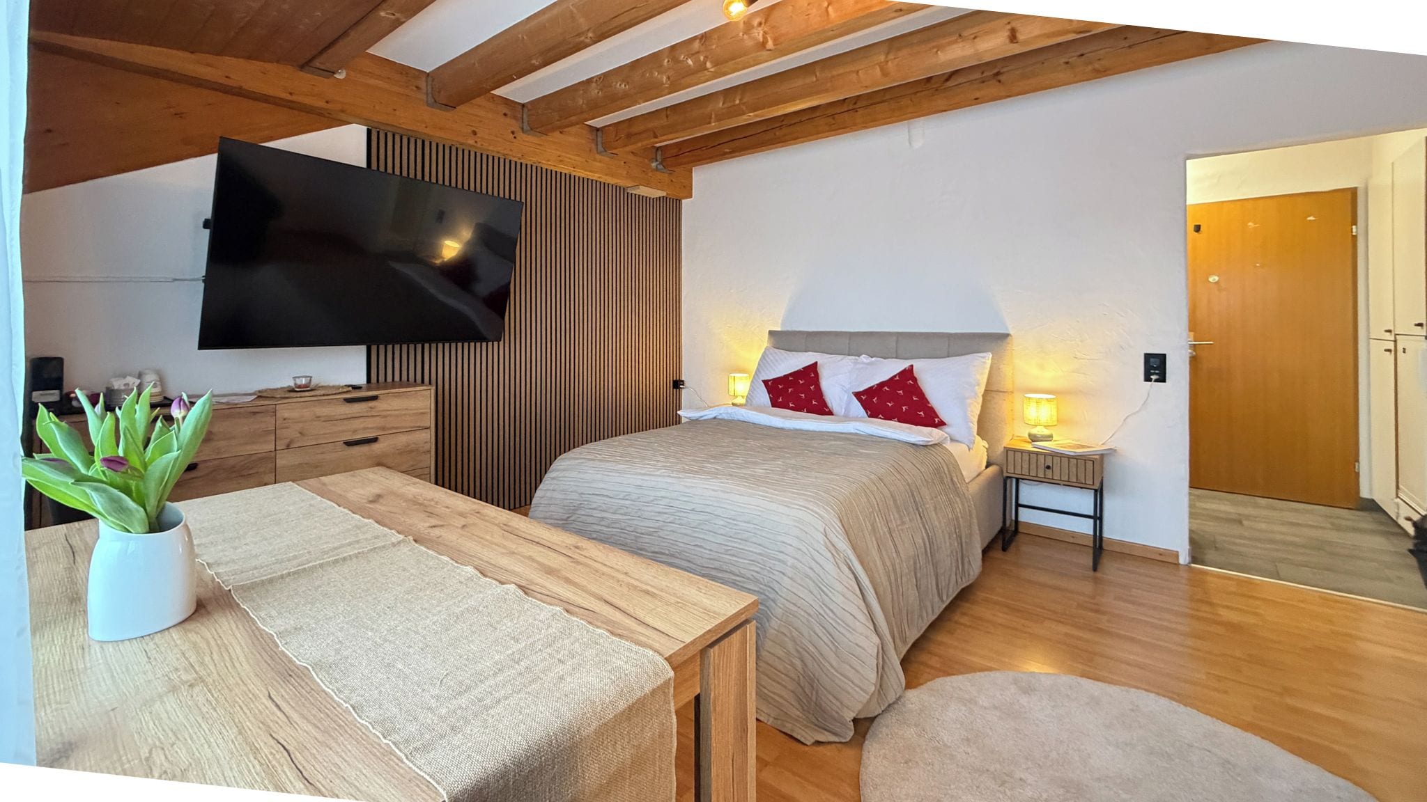 Una camera da letto con un letto, comodini, una TV a parete, un soffitto in legno e una porta.