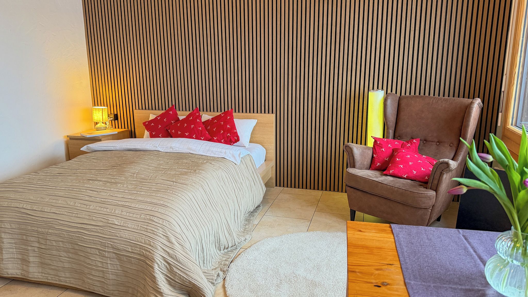 A bedroom with a bed, a nightstand, a chair, and a window.