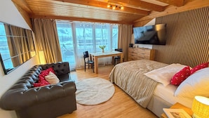 A cozy room with a bed, a sofa, a desk, and a TV. - Plan-B Stay (Samedan)