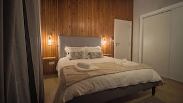 A bedroom with a wooden paneled headboard, a bed with white linens, two bedside lamps, and a door to the right.