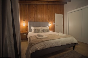 Een slaapkamer met een houten paneel hoofdbord, een bed met witte lakens, twee bedlampen en een deur aan de rechterkant.