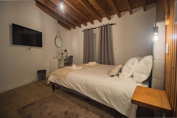 Een slaapkamer met een bed, een bureau, een stoel, een televisie en een houten plafond.