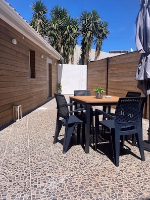 Een terras buiten met een houten tafel en stoelen, omgeven door een houten hek en palmbomen.